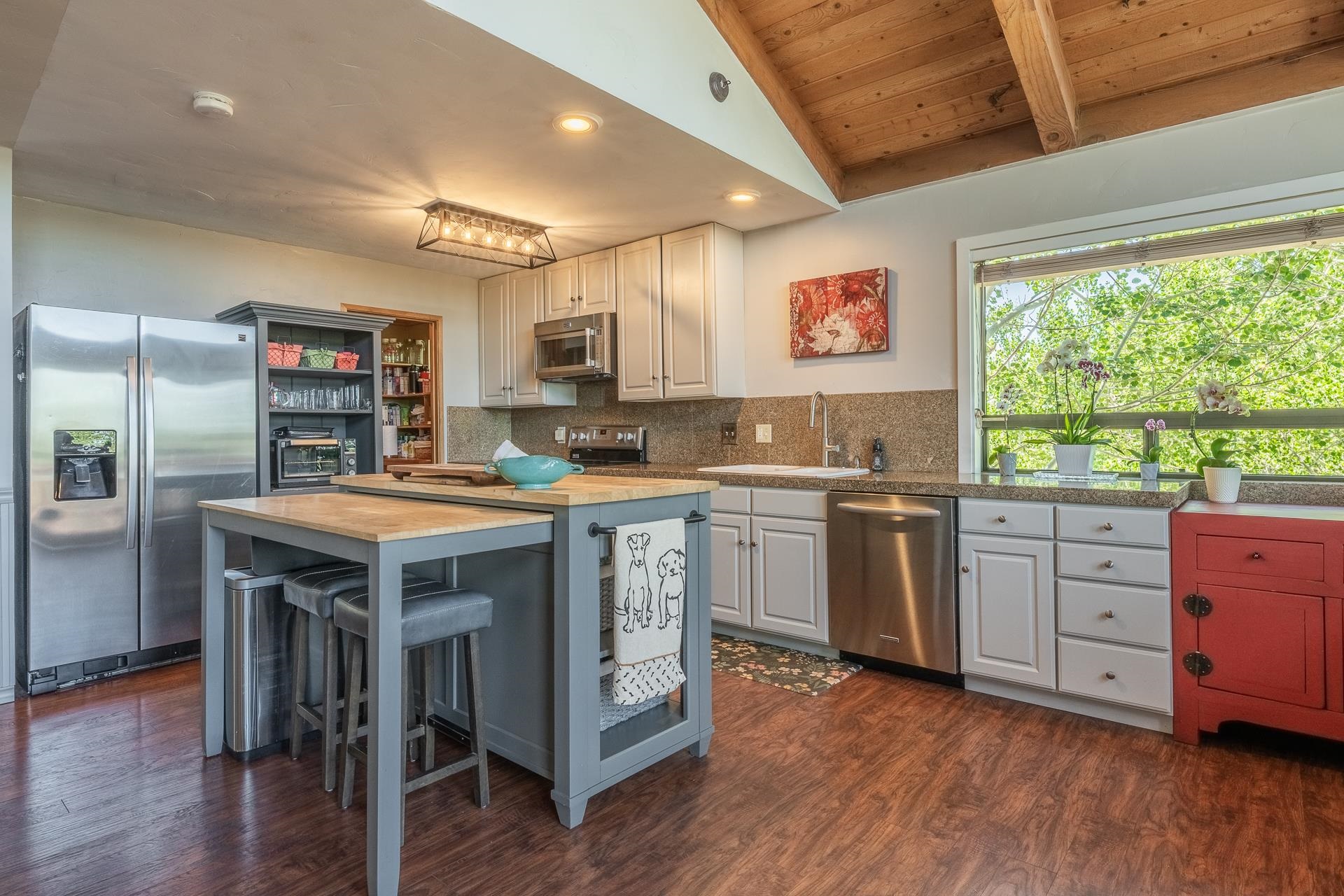 537 Aspen Spring Ranch Road Mammoth Lakes, CA 93546 - Photo 4 of 40 Open-concept kitchen featuring wood-finish flooring, a central island with seating, stainless steel appliances, white cabinetry, and a vaulted wood-paneled ceiling