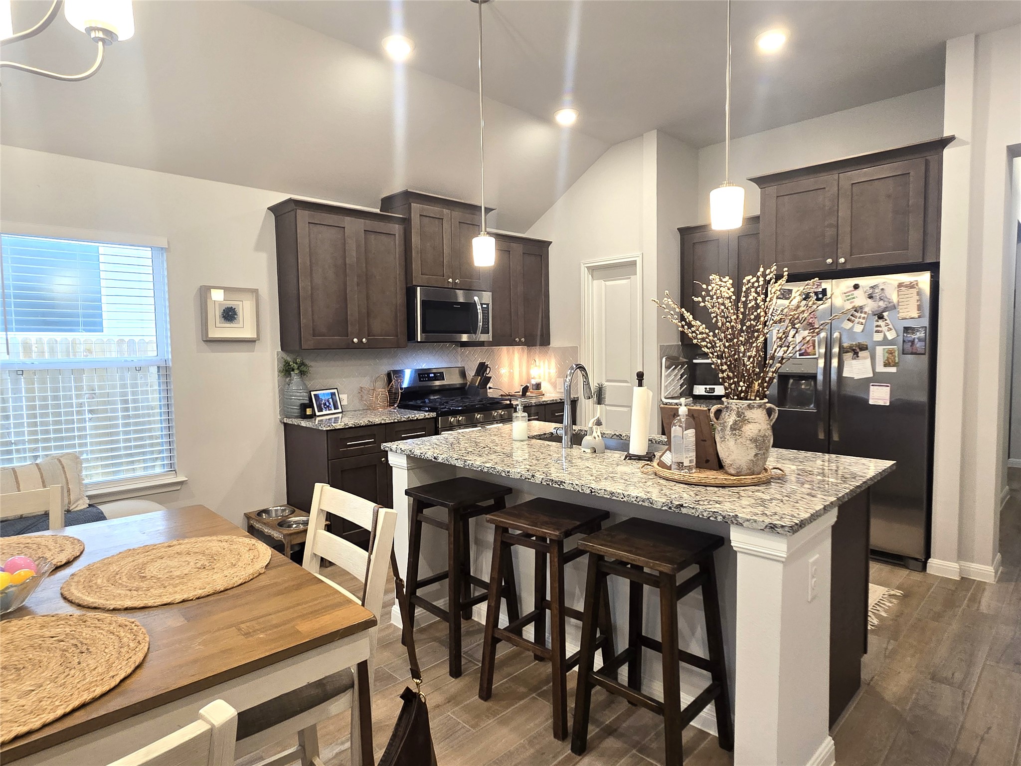133 Boulder Ridge Trail Liberty Hill, TX 78642 - Photo 9 of 32 Kitchen featuring dark wood finish cabinets, stainless steel appliances, light stone countertops, a kitchen bar, and lofted ceiling