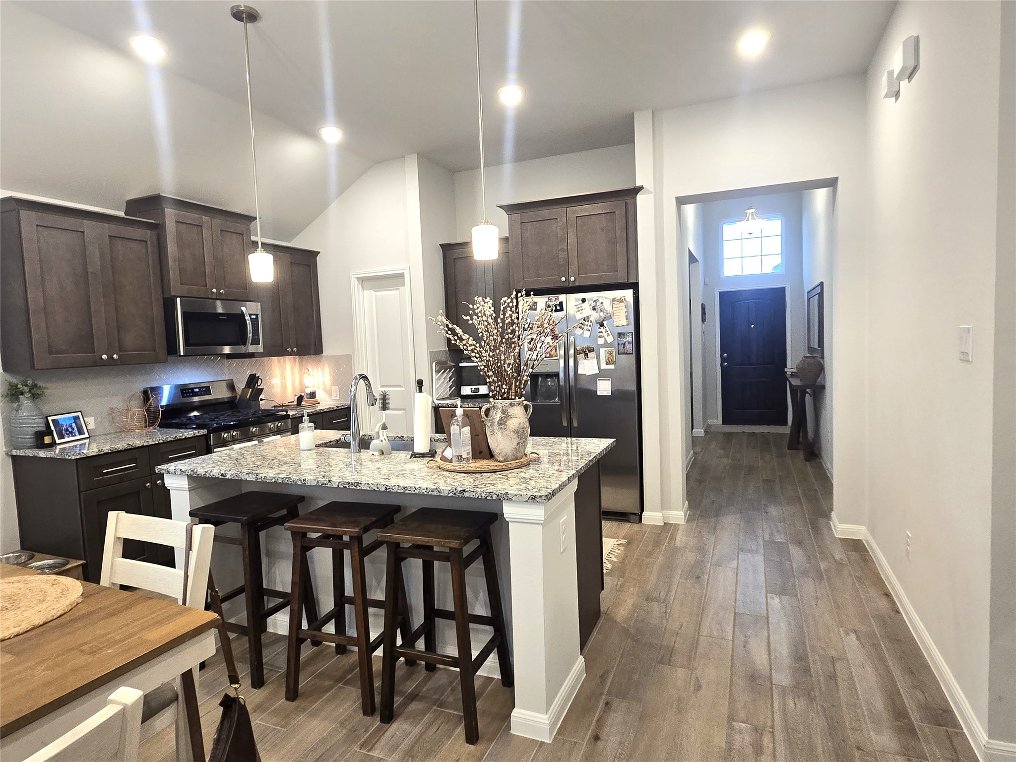 133 Boulder Ridge Trail Liberty Hill, TX 78642 - Photo 11 of 32 Kitchen with a breakfast bar area, light stone counters, stainless steel appliances, dark wood finish cabinetry, and an island with sink