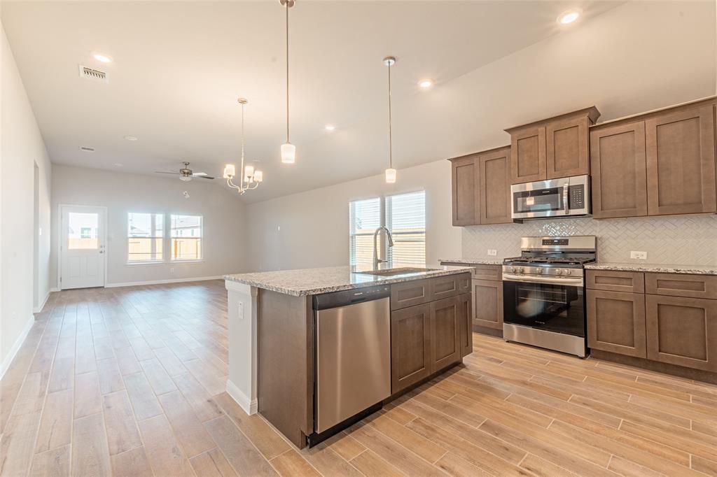 133 Boulder Ridge Trail Liberty Hill, TX 78642 - Photo 32 of 32 Kitchen featuring stainless steel appliances, light stone counters, open floor plan, a kitchen island with sink, and wood tiled floors