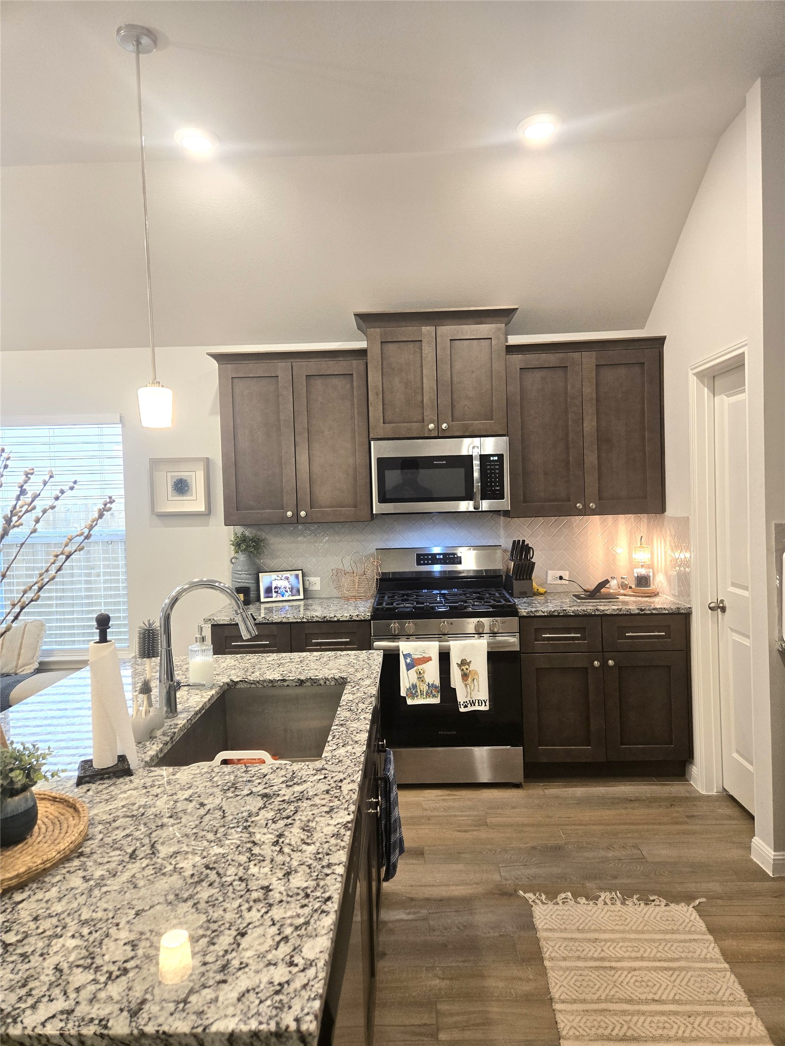 133 Boulder Ridge Trail Liberty Hill, TX 78642 - Photo 6 of 32 Kitchen with dark wood finish cabinetry, stainless steel appliances, lofted ceiling, dark wood-type flooring, and light stone countertops