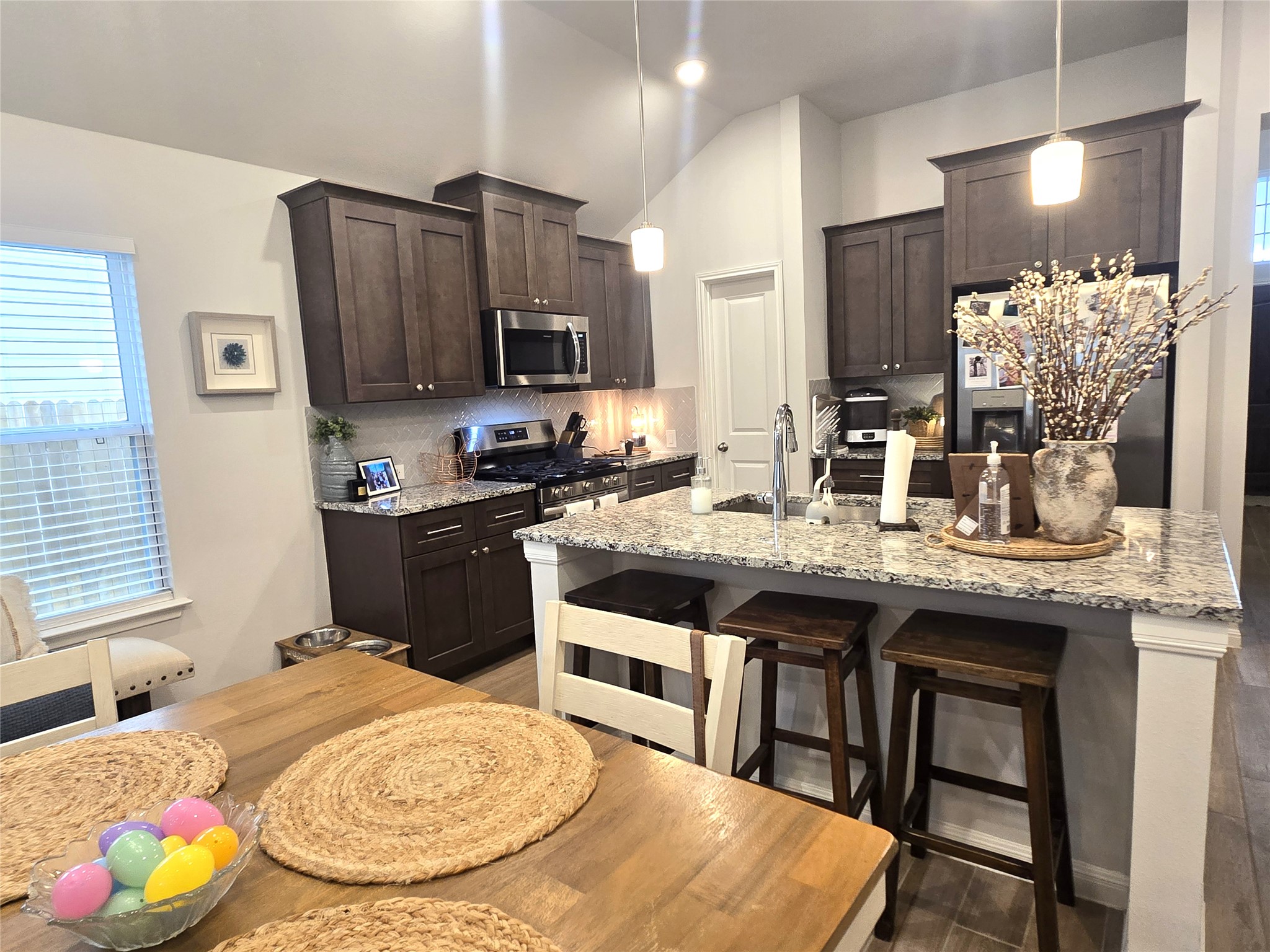 133 Boulder Ridge Trail Liberty Hill, TX 78642 - Photo 7 of 32 Kitchen with dark wood finish cabinetry, light stone countertops, stainless steel appliances, a breakfast bar, and an island with sink