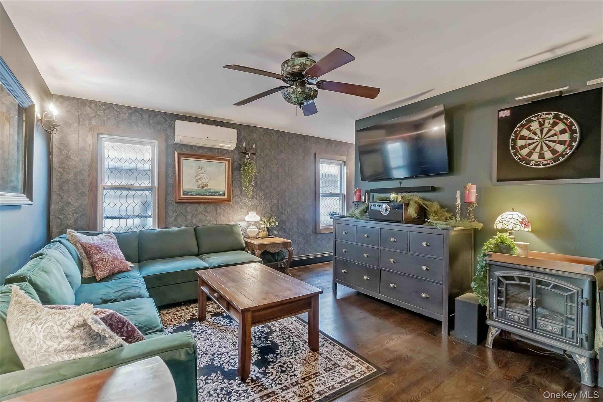 27 West 11th Road Queens, NY 11693 - Photo 3 of 18 Living area featuring a ceiling fan, dark wood-style flooring, wallpapered walls, a wood stove, and a wall mounted AC
