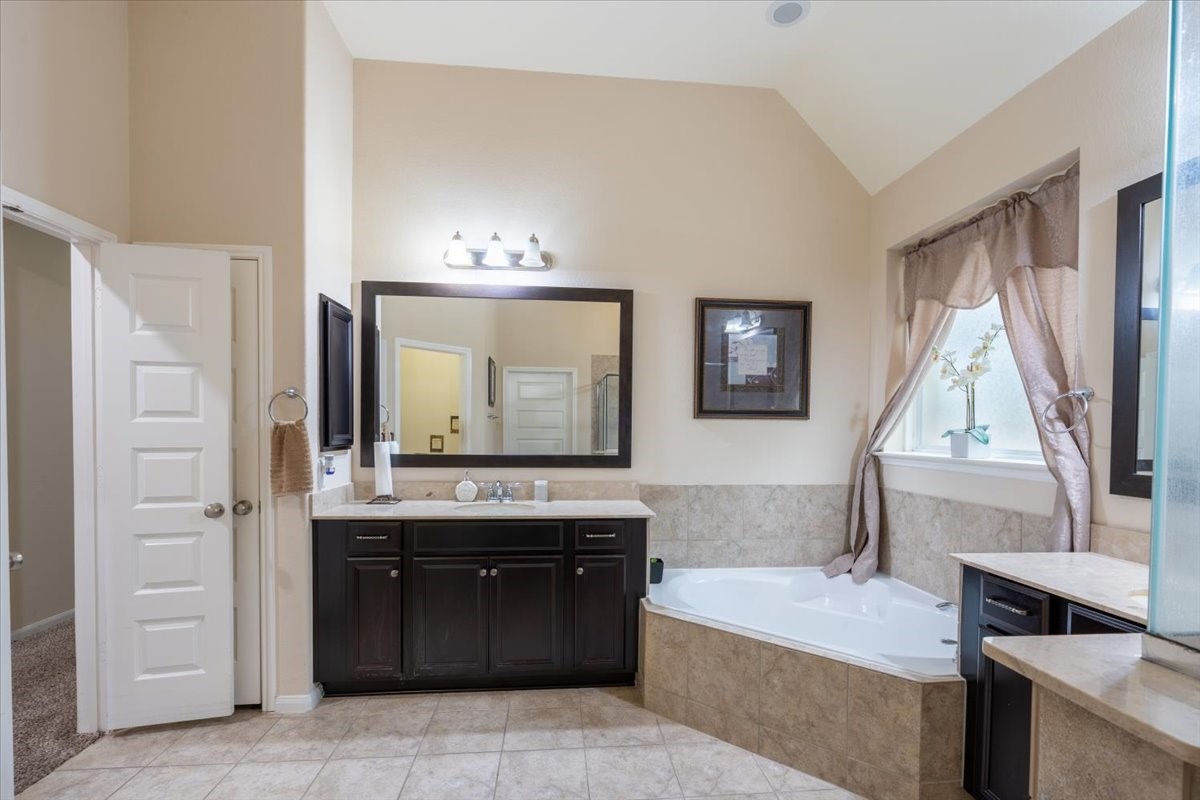 22002 Flashing Ridge Spring, TX 77389 - Photo 18 of 43 This spacious bathroom features a large corner soaking tub, double vanity with dark wood cabinets, and stylish tile flooring. A window provides natural light, complemented by elegant curtains, creating a relaxing and inviting atmosphere.