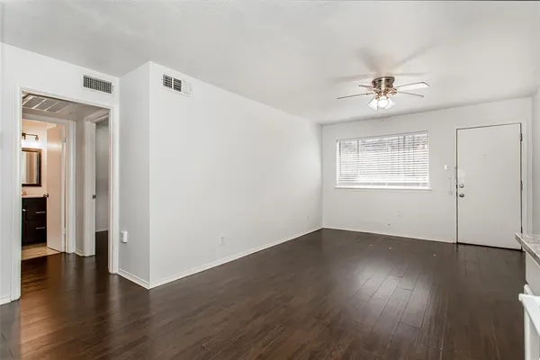 an empty room with wooden floor chandelier fan and windows
