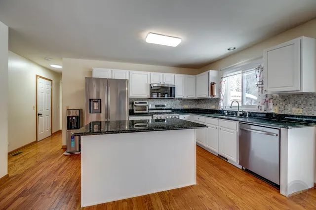 a kitchen with stainless steel appliances granite countertop a refrigerator a sink dishwasher a stove and white cabinets with wooden floor