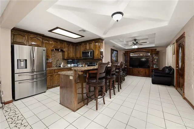 a kitchen with stainless steel appliances kitchen island granite countertop a refrigerator a stove a sink a dining table and chairs with a large window