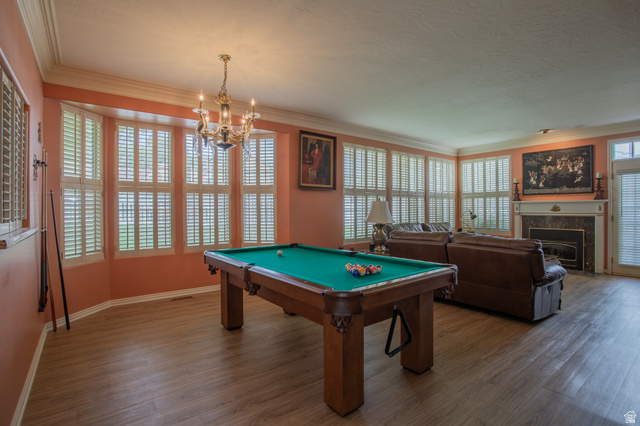 5302 South Birch Pt Road Murray, UT 84117 - Photo 13 of 29 Spacious room featuring wood-finish flooring, a bay window with plantation shutters, an ornate chandelier, and a fireplace with a stone surround