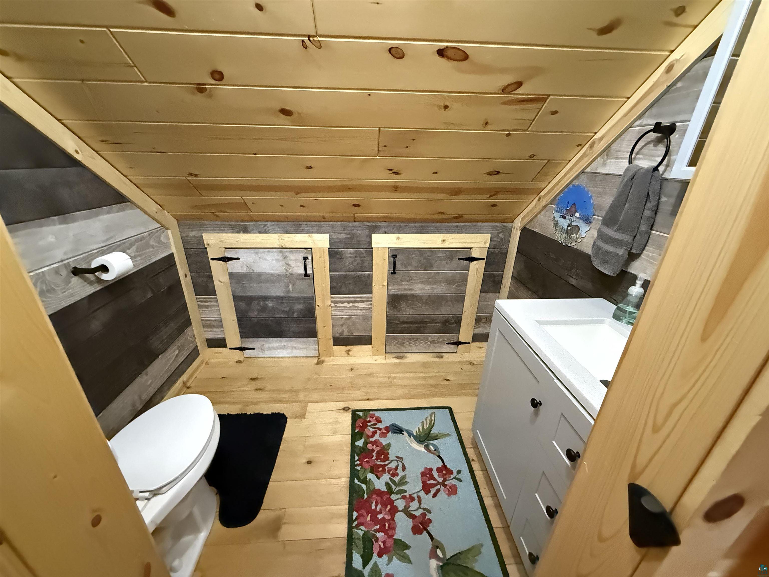 37590 Degerstrom Road Askov, MN 55704 - Photo 30 of 53 Compact bathroom featuring natural wood planking, white vanity with black hardware, and built-in storage access