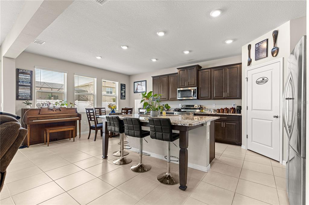 8142 Southwest 59th Avenue Ocala, FL 34476 - Photo 13 of 54 a kitchen with stainless steel appliances kitchen island granite countertop a stove a sink a microwave a dining table and chairs
