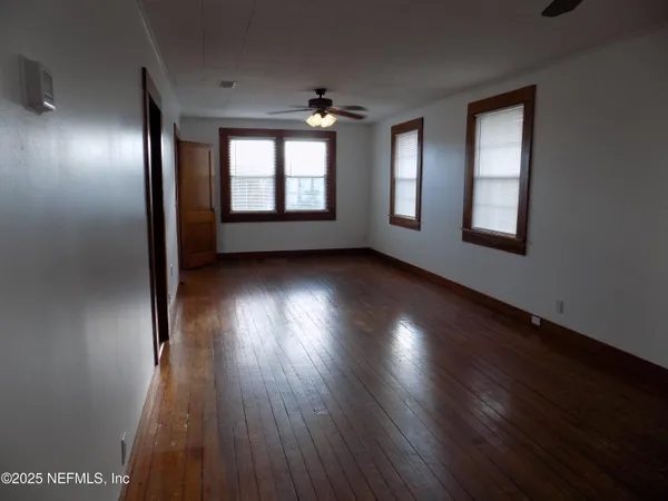 an empty room with wooden floor windows and fan