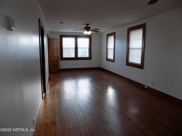 an empty room with wooden floor windows and fan