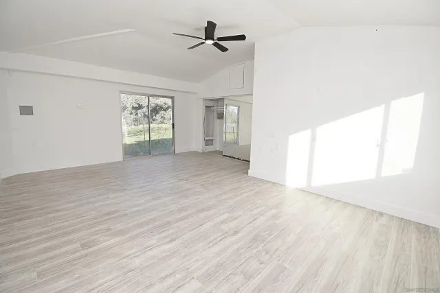 an empty room with wooden floor ceiling fan and windows