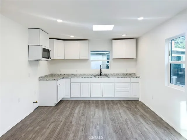 a kitchen with granite countertop white cabinets and white appliances with wooden floor