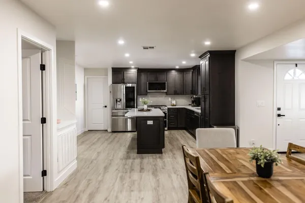 a kitchen with stainless steel appliances kitchen island granite countertop a refrigerator a stove top oven a sink dishwasher and white cabinets with wooden floor