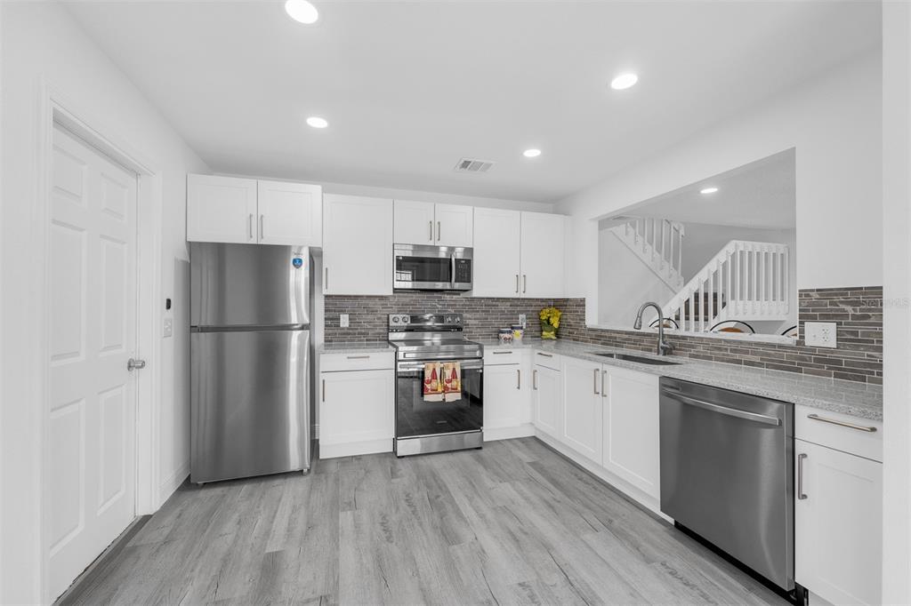 4402 Ring Neck Road, Unit 19B Orlando, FL 32808 - Photo 15 of 35 a kitchen with a refrigerator a sink dishwasher a stove and white cabinets with wooden floor