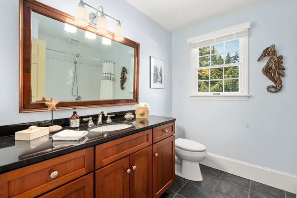 a bathroom with a granite countertop toilet a sink a mirror and a window