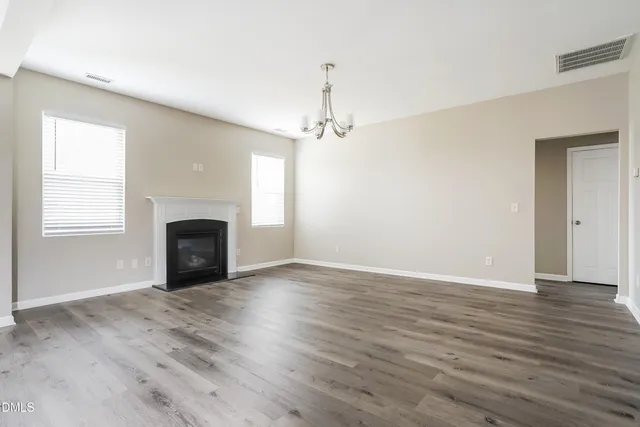 an empty room with wooden floor fireplace and windows