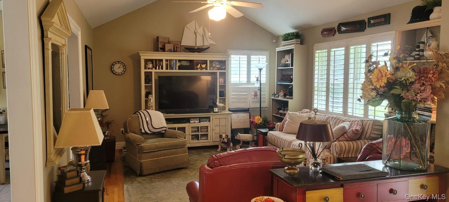 312 Riley Avenue Calverton, NY 11933 - Photo 7 of 30 Spacious living area featuring a vaulted ceiling with a ceiling fan, built-in media console, plantation shutters, and integrated shelving