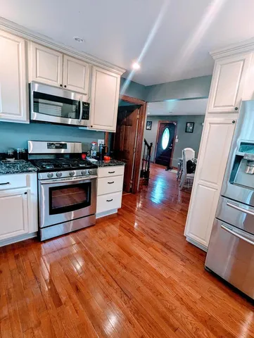 a kitchen with stainless steel appliances granite countertop a stove top oven a sink dishwasher and a microwave with wooden floor