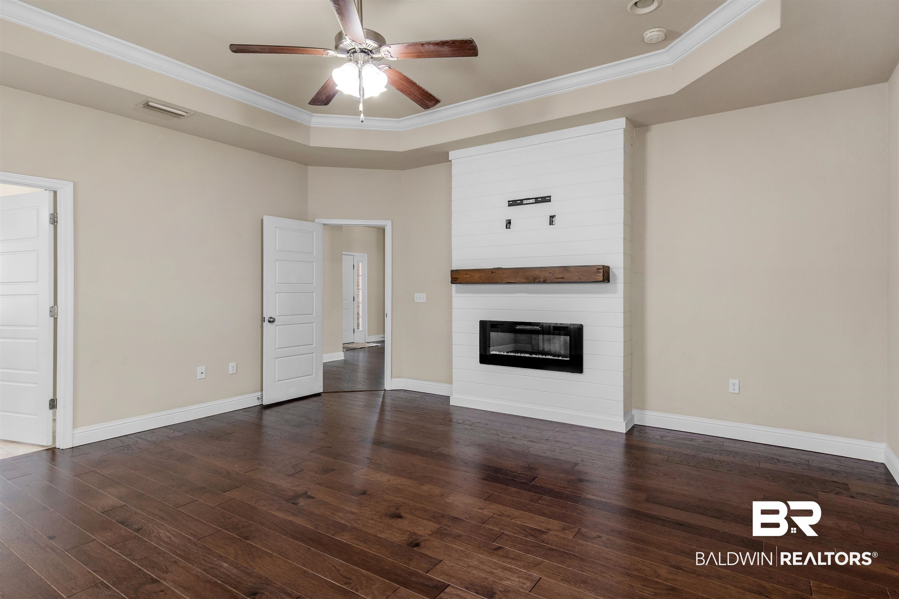 122 Open Field Drive Fairhope, AL 36532 - Photo 6 of 27 Unfurnished living room featuring a fireplace, ceiling fan, a tray ceiling, ornamental molding, and dark wood-type flooring
