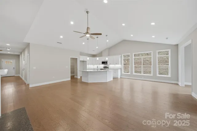 a view of an empty room with wooden floor kitchen view and a window