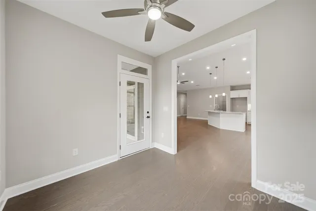 an empty room with fan and way to kitchen