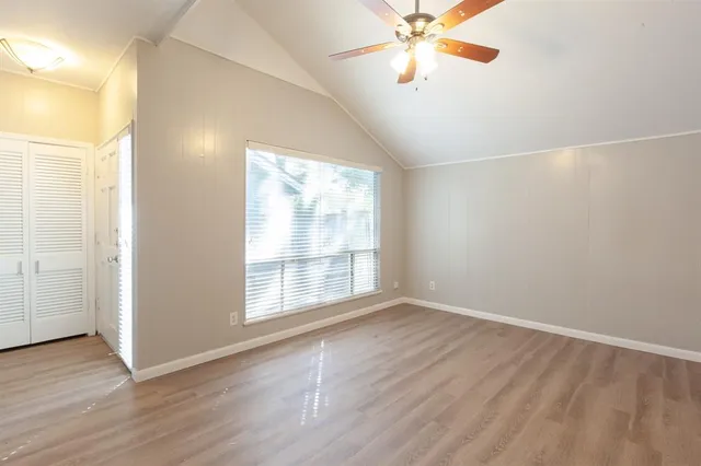 an empty room with wooden floor fan and windows