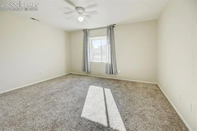 an empty room with a chandelier fan and windows
