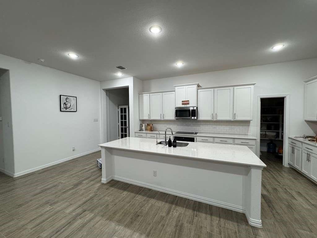 Kitchen with backsplash, white cabinetry, dark wood finished floors, light stone countertops, and stainless steel microwave