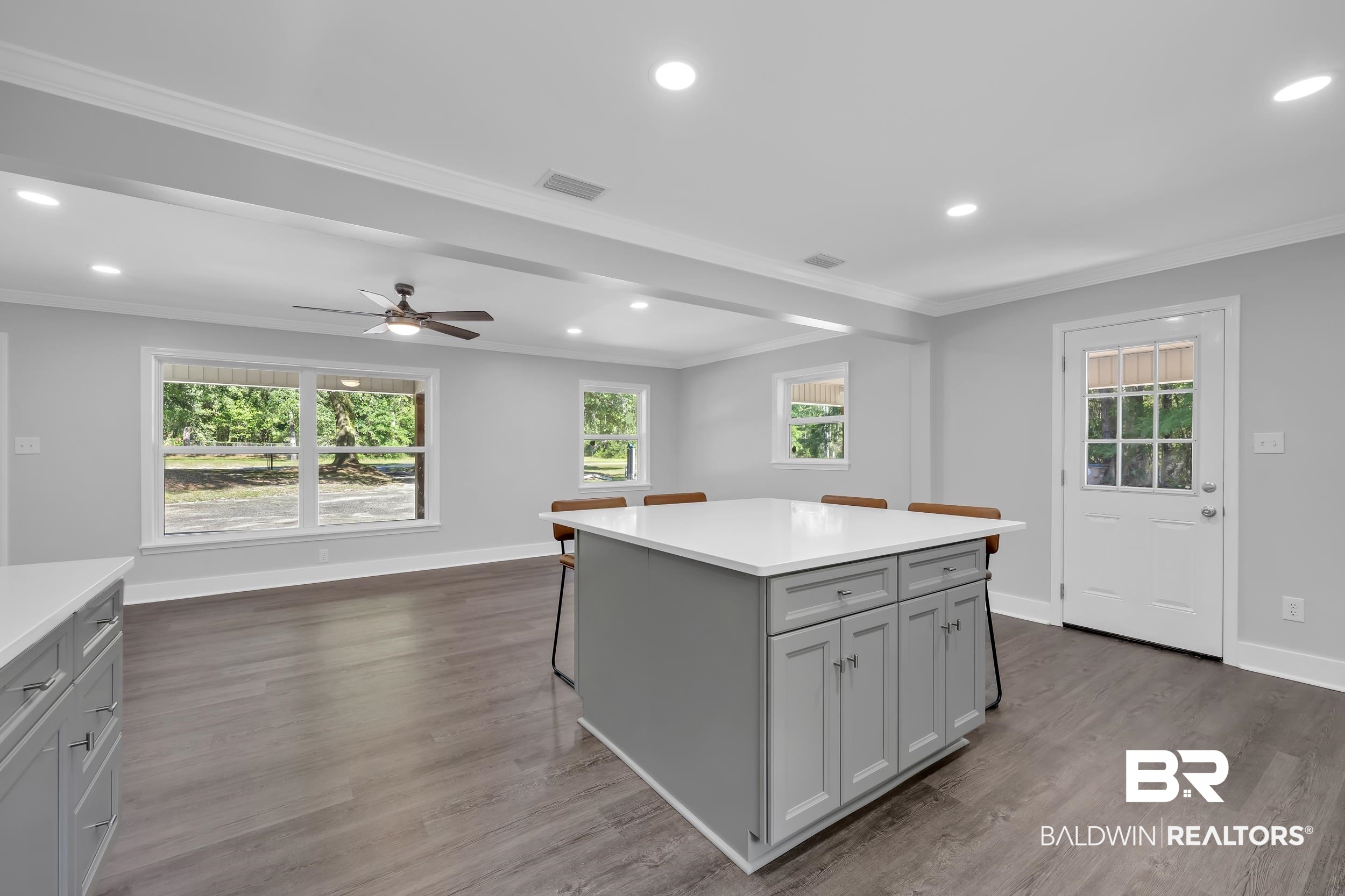 2712 Shelton Beach Rd Extension Mobile, AL 36613 - Photo 11 of 24 Open-concept living space featuring a central kitchen island with a white countertop and gray cabinetry, wood-finish flooring, recessed lighting, a ceiling fan, and multiple large windows