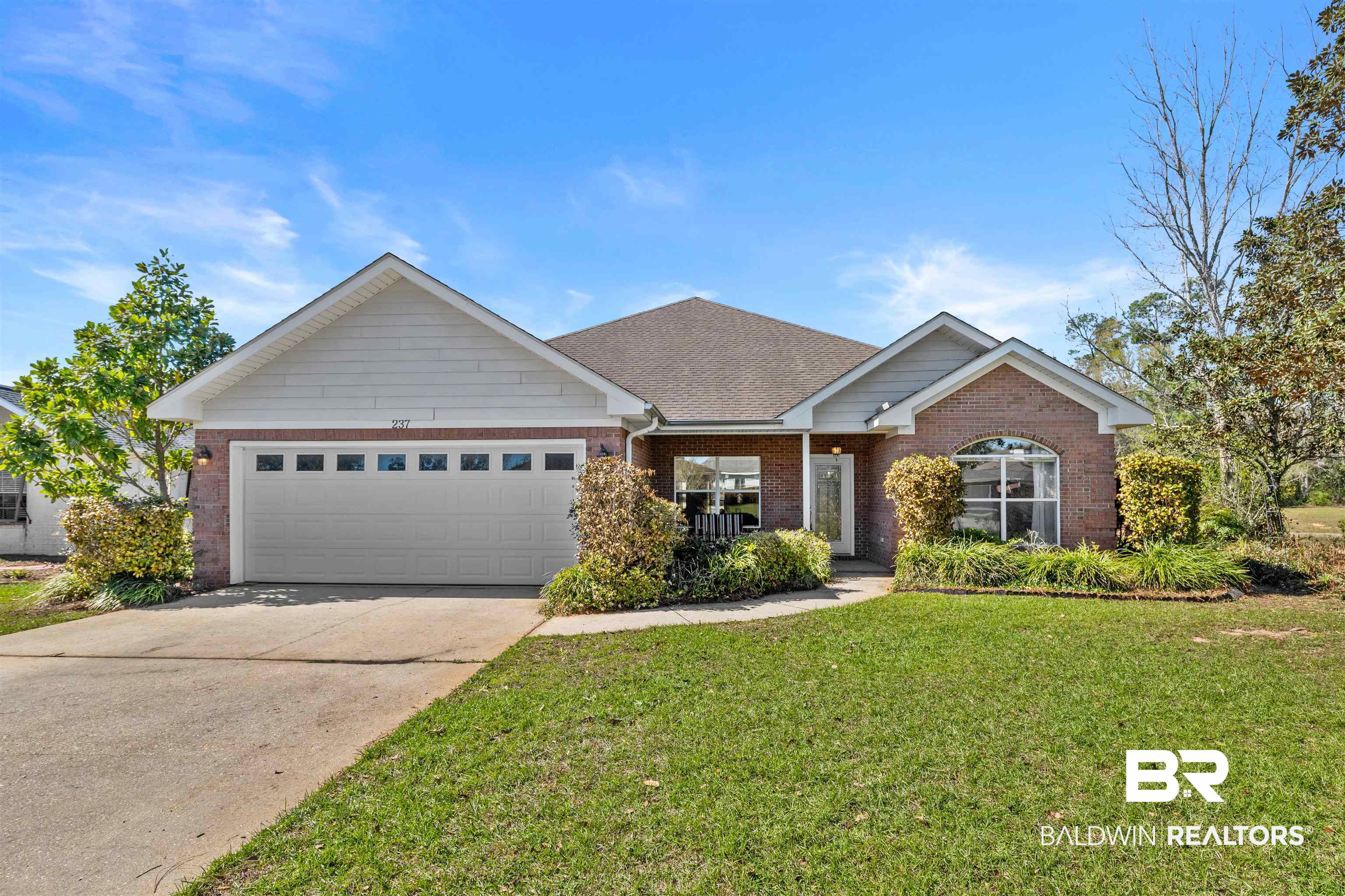 Single story home with driveway, a front yard, a shingled roof, a garage, and brick siding