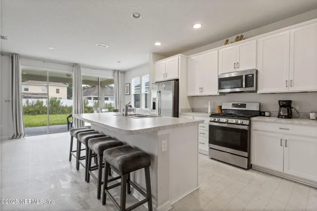 a kitchen with stainless steel appliances granite countertop a stove a sink a microwave a refrigerator and white cabinets