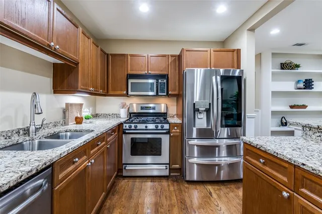 a kitchen with stainless steel appliances granite countertop a stove a sink dishwasher a refrigerator and a oven with wooden floor