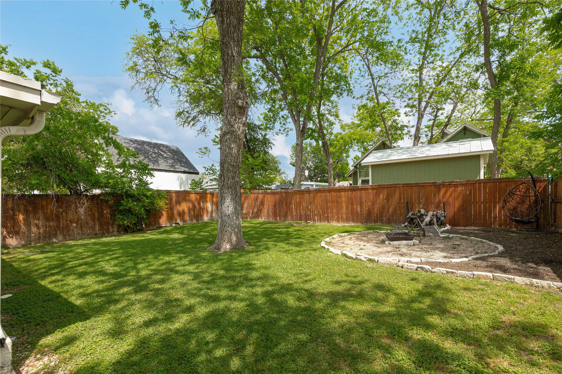 4607 Evans Avenue, Unit B Austin, TX 78751 - Photo 23 of 34 Expansive green lawn featuring a stone-rimmed fire pit area, mature trees, and a privacy fence