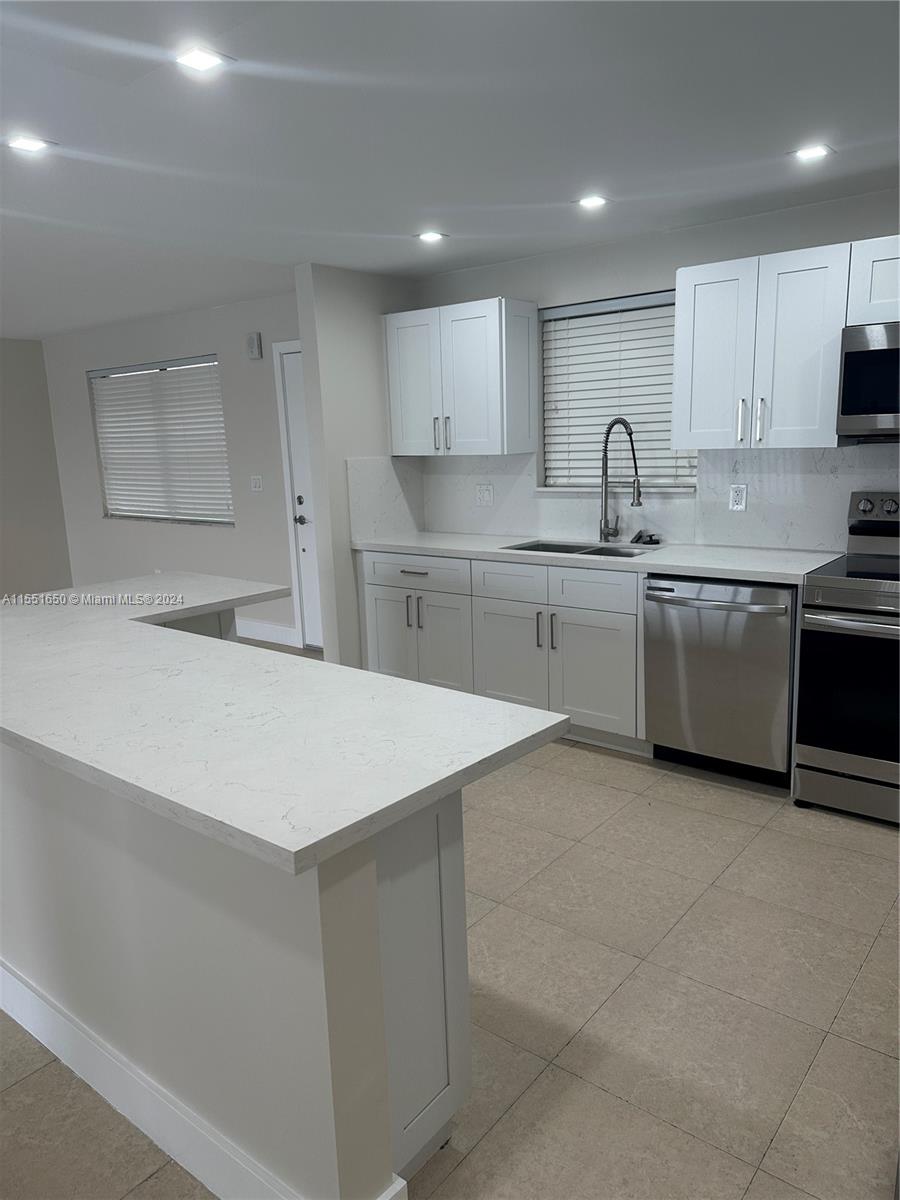 a kitchen with stainless steel appliances a sink dishwasher stove refrigerator and white cabinets with wooden floor