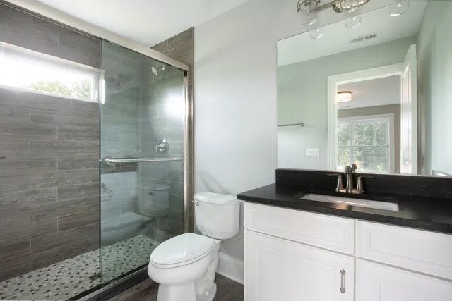 a bathroom with a granite countertop sink a toilet a mirror and shower