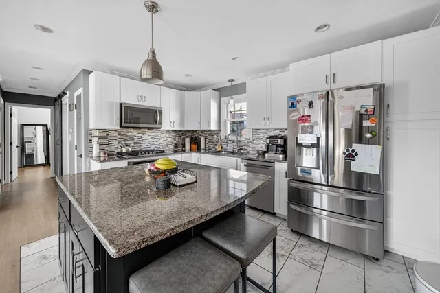 a kitchen with granite countertop a refrigerator a stove a microwave oven a sink dishwasher and white cabinets with wooden floor