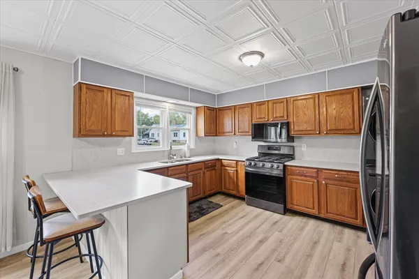 a kitchen with stainless steel appliances granite countertop wooden cabinets a sink dishwasher a stove and a refrigerator with wooden floor