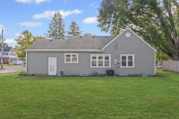 a house that is sitting in the grass with large trees and plants