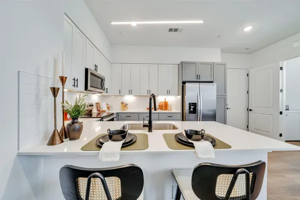 a kitchen with stainless steel appliances kitchen island granite countertop a dining table chairs refrigerator and sink