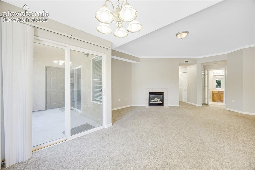 3864 Riviera Grove, Unit 102 Colorado Springs, CO 80922 - Photo 8 of 24 Spacious room featuring neutral carpeting, a fireplace with a white tile surround, and crown molding