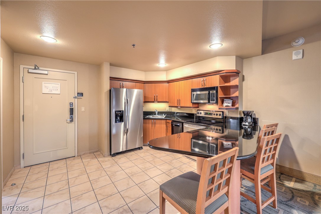 211 East Flamingo Road, Unit 1402 Las Vegas, NV 89169 - Photo 6 of 43 Kitchen with dark countertops, appliances with stainless steel finishes, brown cabinets, open shelves, and a breakfast bar