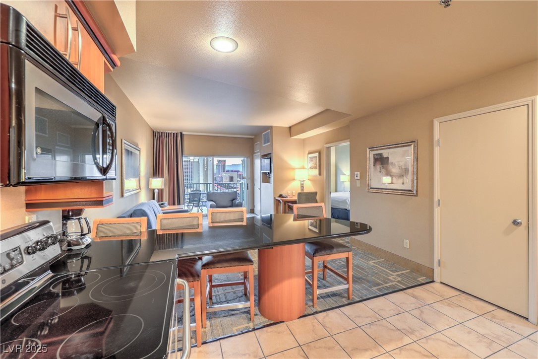 211 East Flamingo Road, Unit 1402 Las Vegas, NV 89169 - Photo 8 of 43 Kitchen featuring stainless steel electric stove, a kitchen bar, light tile patterned floors, dark countertops, and a peninsula