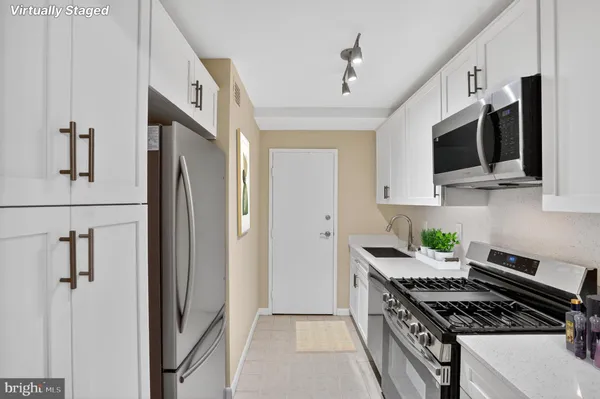 a kitchen with stainless steel appliances a stove a microwave a refrigerator a sink and white cabinets