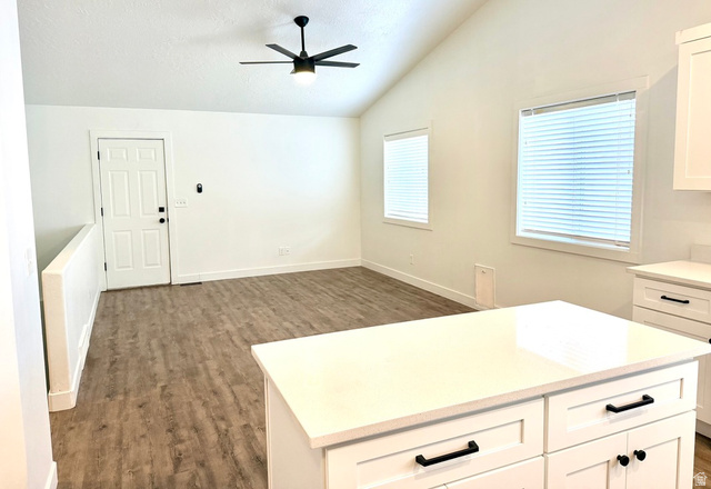 11895 Inauguration Road Draper, UT 84020 - Photo 4 of 10 Vaulted ceiling with a ceiling fan, wood-finish flooring, multiple windows with blinds, and a kitchen island with white cabinetry and dark hardware