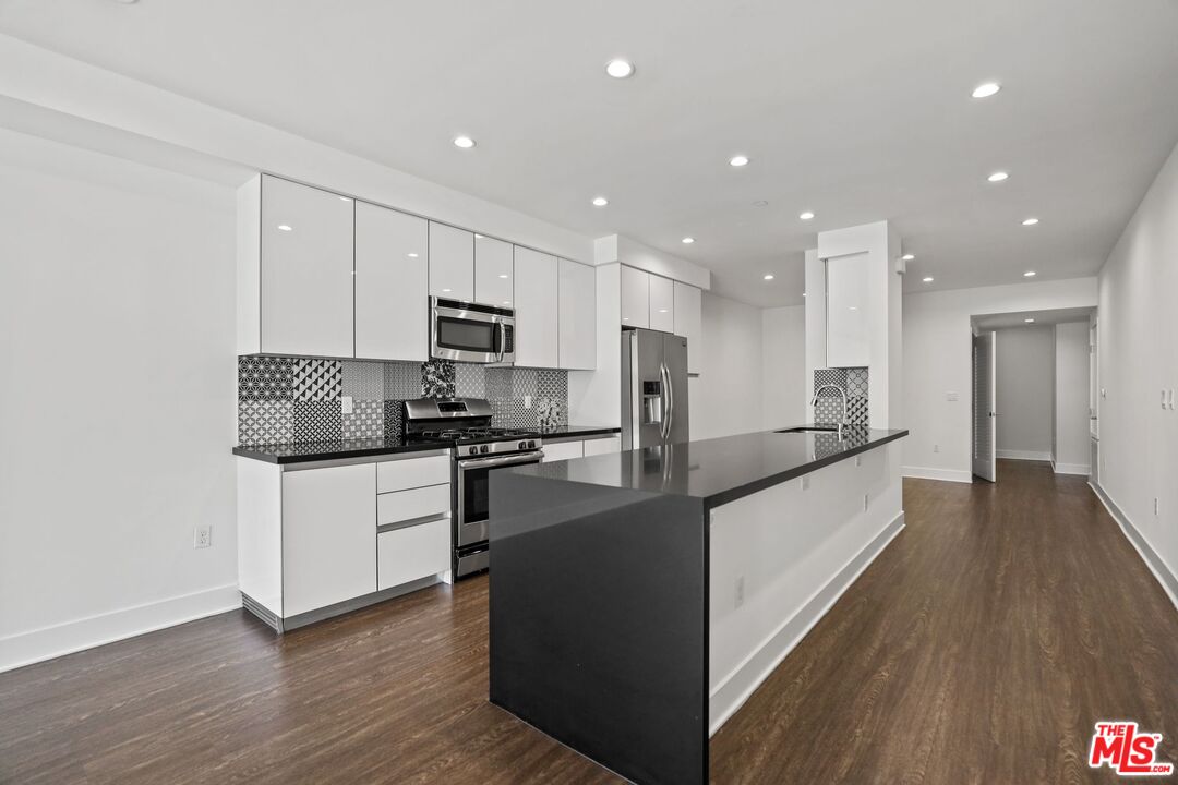 a large kitchen with a center island wooden floor stainless steel appliances and a window