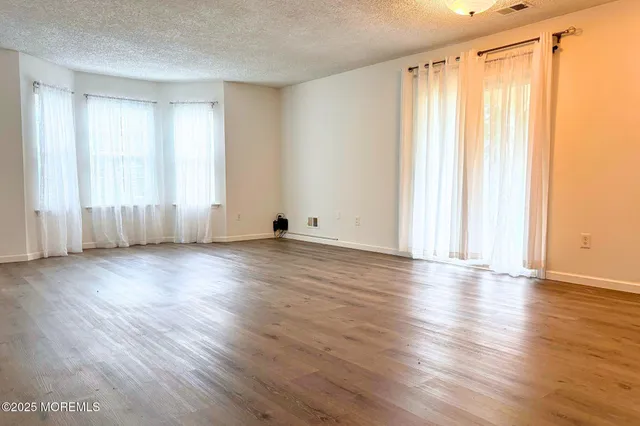 an empty room with wooden floor and windows with curtains