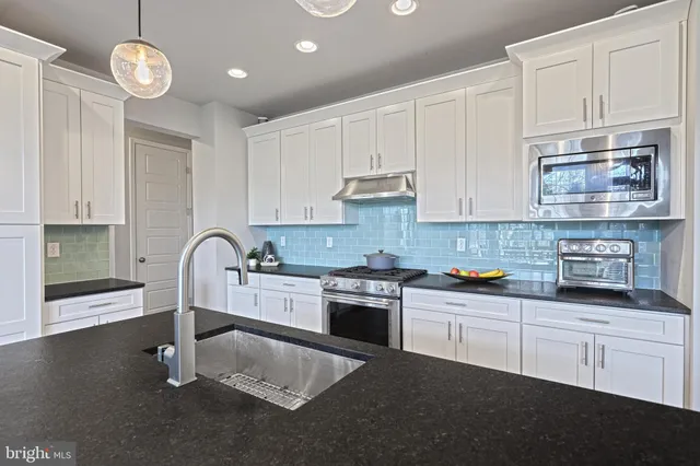 a kitchen with stainless steel appliances granite countertop a stove a sink dishwasher and white cabinets with wooden floor