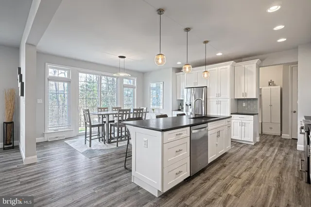 a kitchen with stainless steel appliances granite countertop a stove a sink dishwasher a refrigerator and white cabinets with wooden floor